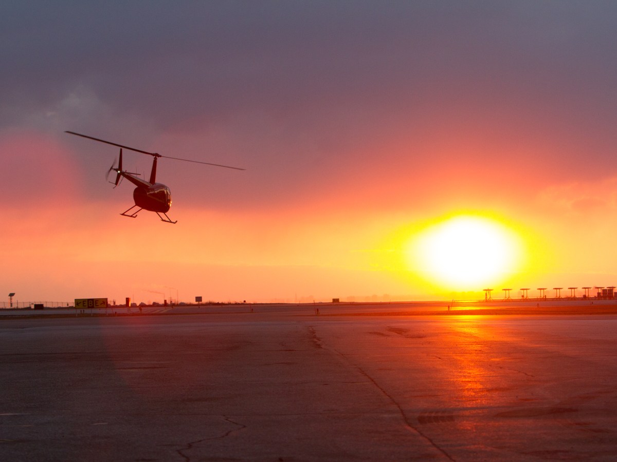 Helicopter taking off at sunset with bright sun and cloudy sky.