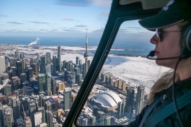 Helicopter view of a snowy cityscape with skyscrapers and a large tower on a clear day.