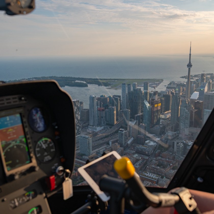 Aerial view of city skyline from helicopter cockpit showing water and tower.