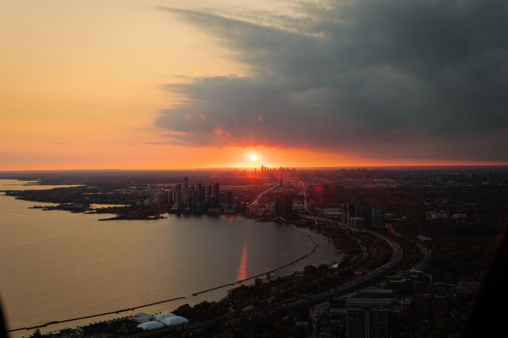 Sunset over city skyline and water, with clouds and orange sky.