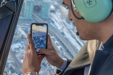 Person in a helicopter taking a cityscape photo with a smartphone.